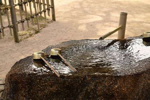 Bamboo Fountain with drinking water falling onto a large rock with water ladles - Japanese Garden
